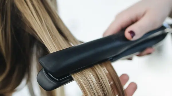 Stylist smoothing a section of highlighted hair with straighteners in a salon